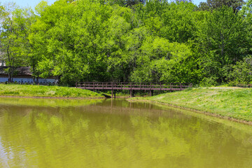 a brown wooden bridge over a silky green lake surrounded by lush green trees, grass and plants in Marietta Georgia USA