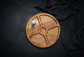 Wall Mural - round wooden board for serving food and a sieve with sugar on a black table, top view