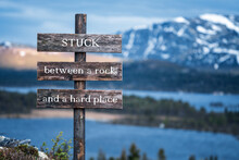 Stuck Between A Rock And A Hard Place Text Quote Written On Wooden Signpost Outdoors In Nature With Lake And Mountain Scenery In The Background. Moody Feeling.