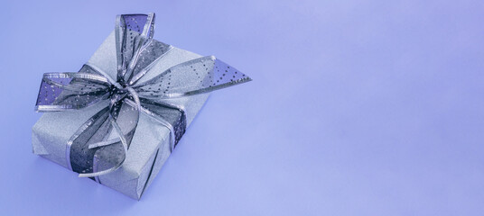 Wall Mural - Beautiful silver gift with black ribbon on purple background. Christmas present background.