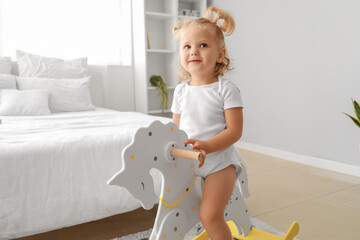 Adorable baby girl with rocking horse at home