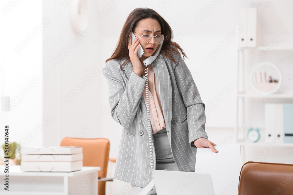 Busy young secretary talking by phones in office