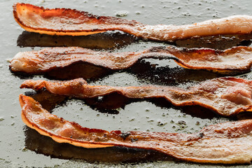 Wall Mural - sizzling bacon frying on a griddle pan.