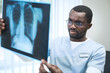 © Mediaphotos - Concentrated young Afro-American doctor in eyeglasses and uniform analyzing CT scan of chest of coronavirus patient