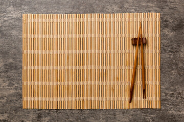 Wall Mural - Two chopsticks and bamboo mat on cement background. Top view, copy space