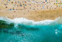 Aerial Shooting From A Drone On A Sandy Beach With People Sunbathing And Relaxing. Flat View Of The Shore And Turquoise Waves Of The Surf And People Bathing
