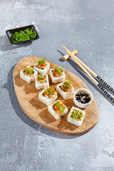 Wall Mural - Maki roll with fried carrot and green onion top on wooden board in contemporary composition. Sushi roll with chopsticks on concrete table. Maki sushi in minimal style.