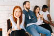 © dikushin - Tired excited female job candidates looking at camera while waiting interview with hr sitting in queue line row with bored diverse multi-ethnic candidates, on background of white brick wall.