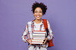 © ViDi Studio - Young smiling fun girl woman of African American ethnicity teen student in shirt backpack hold pile of books isolated on plain purple background. Education in high school university college concept.