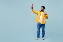 Full Body Fun Young Man Of African American Ethnicity Wear Yellow Shirt Doing Selfie Shot On Mobile Cell Phone Post Photo On Social Network Show V-sign Isolated On Plain Pastel Light Blue Background.
