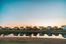 A Row Of Suburban Houses Overlook A Small Pond During Sunset With Room For Copy