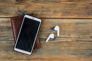 Smartphone, earphone and brown leather wallet on wood table background. Hipster modern life style layout for inserting text