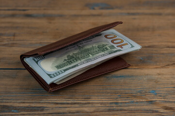 Wall Mural - Brown leather wallet with one hundred dollar bills on wooden table. Top view