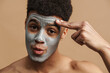 © Drobot Dean - Surprised shirtless man with cosmetic clay mask touching his forehead