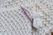 Top view of a ball of yarn, 5 mm purple crochet hook, yellow measuring tape, pink marker on a partially finished white cotton blanket, original raised crochet stitch pattern. Handmade creativity