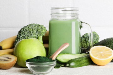 green smoothie in glass bottle, spirulina powder, vegetables and fruits on white ceramic tile background. healthy, raw, vegan diet concept. copy space