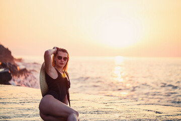 Wall Mural - Beautiful lady in a black swimsuit on the seashore, Smiling face. Golden sunset light