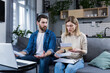 © Liubomir - Young family, husband and wife, reviewing their bills, loan and mortgage agreements, sitting on the couch at home, working with documents on a laptop, embarrassed, upset