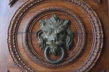 A lion-faced Door knocker on a very ornate old wooden door