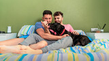 Fototapeta Na drzwi - Modern homosexual family with their black pet dog in bed relaxing and enjoying the sunny day