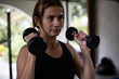 © Amilciar - Concentrated Latin American woman lifts dumbbells during workout at the gym. Healthy lifestyle concept.