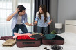 stressed couple having problem with packing clothes into a suitcase on bed at home, holiday travel concept