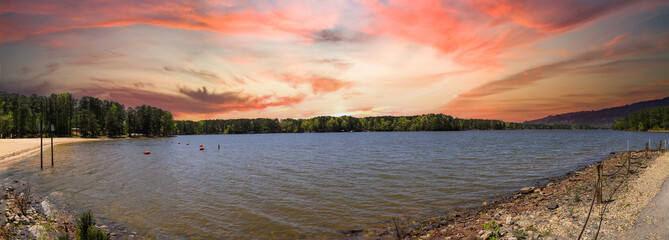 Wall Mural - a stunning panoramic shot of the vast rippling green waters of a lake surrounded by lush green trees with powerful clouds at sunset at Dallas Landing Park in Acworth Georgia USA