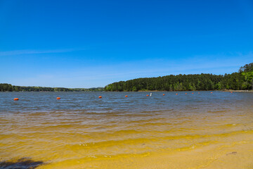 the clear rippling waters of Lake Acworth with waves rolling into the silky brown sand of the beach with red buoys in the water surrounded by lush green trees at Dallas Landing Park in Acworth 