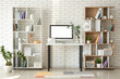 © Pixel-Shot - Workplace with computer, plant branches in vase and shelving units near white brick wall