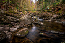 Moss Stones In The River With Suspension Bridge In A Mountain Valley And Green Forest. Natural Landscape Torrent Buchberger Leite In The Bavarian Forest, Germany.