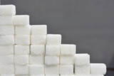 Fototapeta  - Steps made from sugar cubes. Pile of sugar cubes on a grey shiny surface, sugar pyramid.
