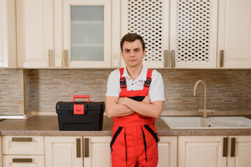 Wall Mural - young man in red overall plumber in a kitchen preparing for fixing water tap.