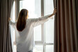 © thebigland45 - A beautiful woman opens the curtains and looks through the window. People and concept of morning.