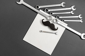 Wall Mural - Father's Day Holiday Concept. Top view of retro stylish black funny paper moustache and combination wrenches on grey and white studio background wall. Copy space for inscriptions