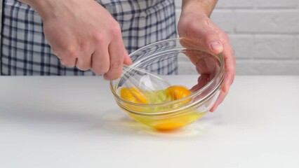 Wall Mural - Male hands beat eggs in a glass bowl a whisk on a white table.