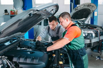 Wall Mural - Two handsome mechanics in uniform are working in auto service. Car repair and maintenance.