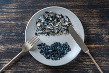 Whole Sunflower Seeds As Well As Sunflower Seed Husks In A Plate Along With A Fork And Knife, Top View, Close Up