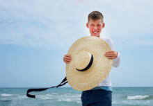 A Boy On The Seashore With A Big Straw Hat. The Face Is Lit Up With A Smile. Positive Vibes. Sea Waves. Ocean. Sand Beach.