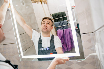 repairman hangs a modern electronic bathroom mirror.