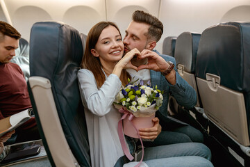 Wall Mural - Happy couple in love showing heart symbol in airplane