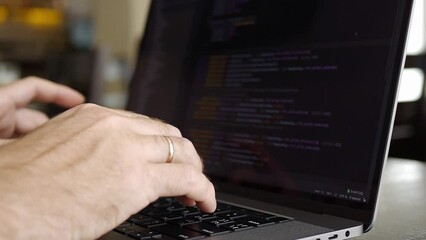 Close-up of male hands typing code on silver notebook keyboard. A caucasian young man works on a laptop in a cafe or coworking space