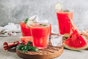 Wall Mural - Watermelon lemonade with lime and fresh basil leaves on concrete background. Refreshing summer drink