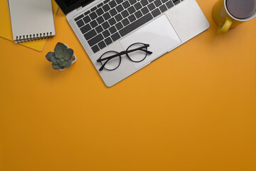 Wall Mural - stylish workplace with computer laptop, notepad, glasses and coffee cup on yellow background. top vi