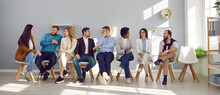 Narrow Wide Shot Of Diverse Employees Sit On Chairs In Row Brainstorm Or Discuss Ideas. Banner Of Smiling Multiethnic Candidate In Line Before Office Meeting Or Interview. Employment Concept.