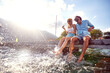 Attractive couple laughing while sitting on jetty near water. Splashing water with legs. Couple in love. Tourism, summertime, togetherness, lifestyle concept.