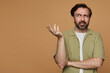 studio portrait of bearded man posing over beige background raised his hand with confused facial expression