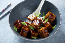 Bowl With Fried Tofu Cubes In Teriyaki Sauce, Middle Close-up On A Light-blue Stone Background, Horizontal Shot
