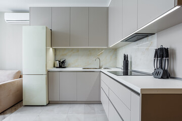 Modern beige and gray stylish kitchen with a table, soft chairs, a sofa and a beige refrigerator. Floor tiles and laminate. Built in household appliance