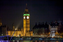 The Clock Of Elizabeth Tower (Big Ben) Illuminated In White And Green Alongside The Palace Of Westminster (Houses Of Parliament) By Night.