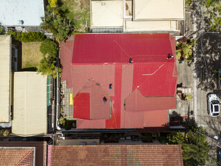 A team of roofers or carpenters installs new corrugated metal roofing with ribbed sheet design on a two storey house. Using a safety harness for protection. Replacing older roof.